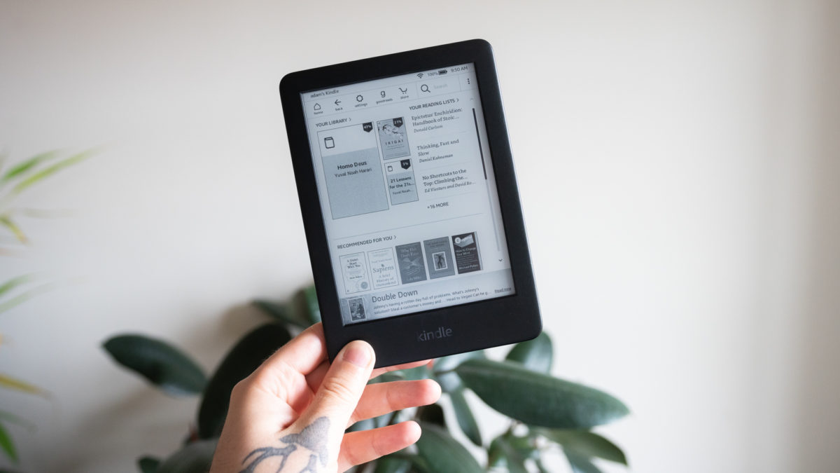 Man holding Kindle against white wall with plants in the background