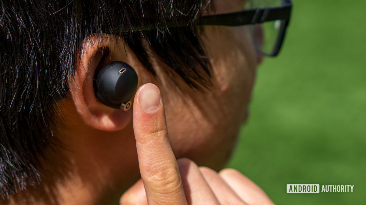 A woman putting her finger up to the Sony WF-1000XM4 earbud.