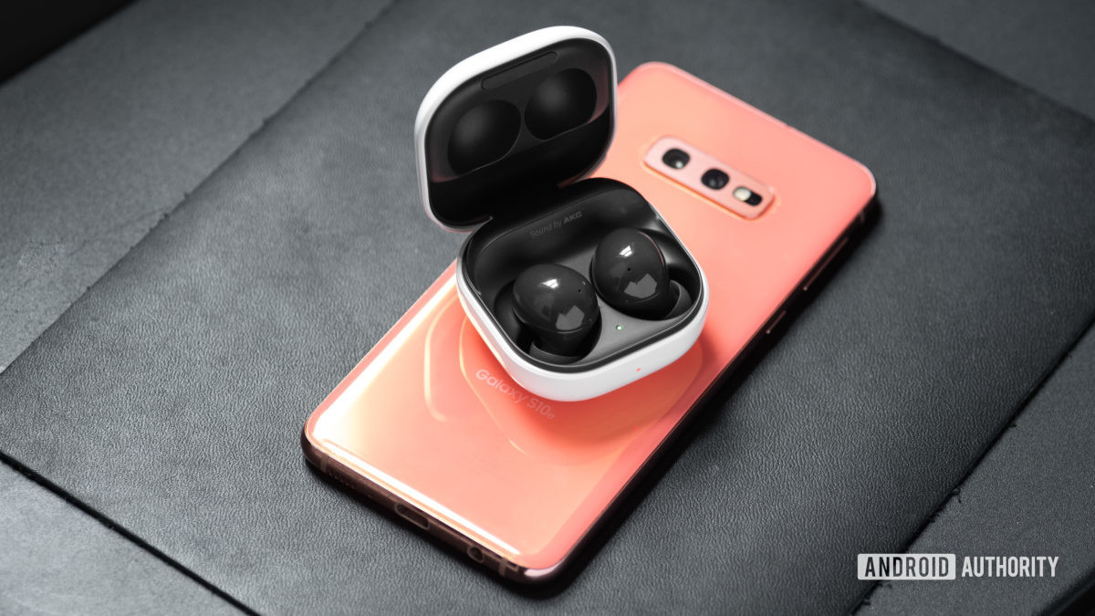 The Samsung Galaxy Buds 2 noise cancelling true wireless earphones in the open charging case on top of a Samsung Galaxy S10e smartphone in pink.