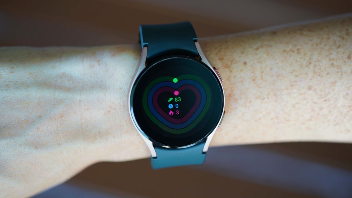 A Galaxy Watch 4 displays the Daily Activity screen hovering over a brown picnic table.