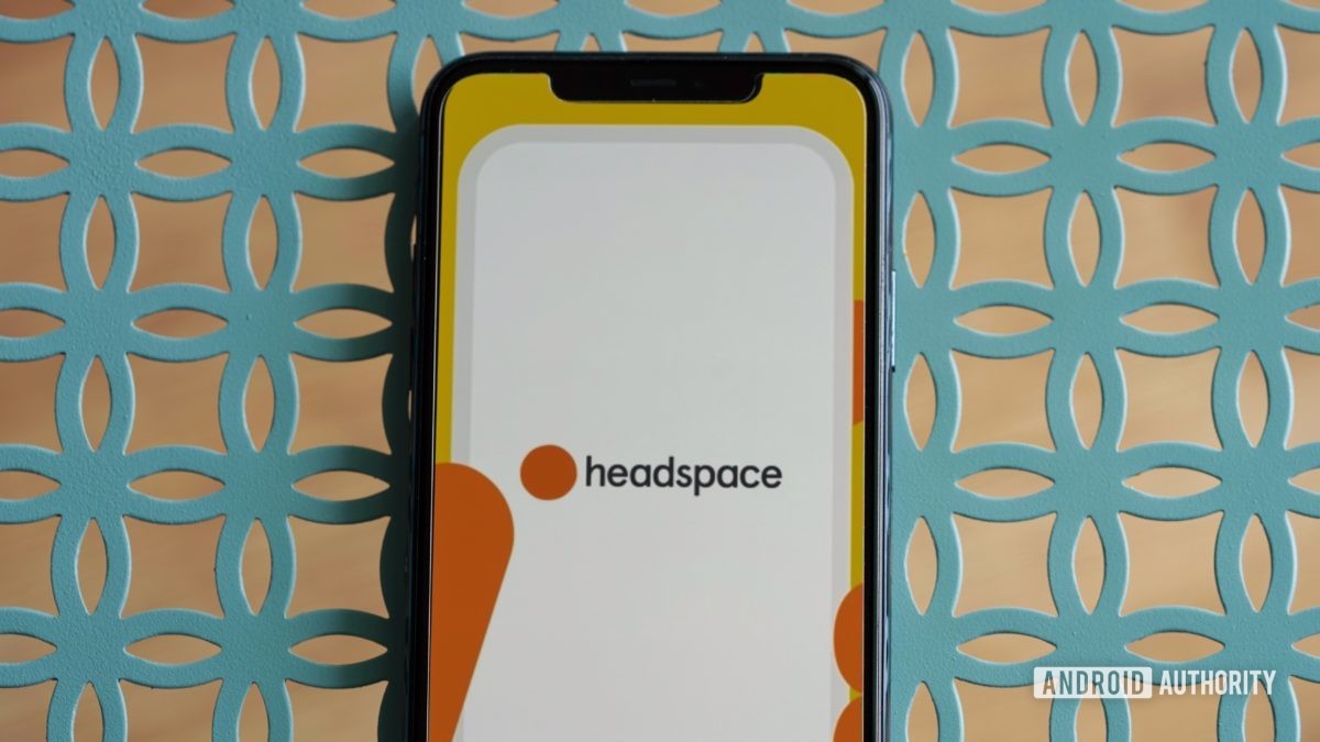 An iPhone 11 rests on a teal metal table, displaying the Headspace app logo.