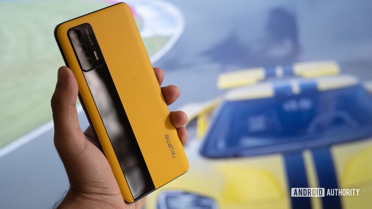 Realme GT in hand with race car behind it.