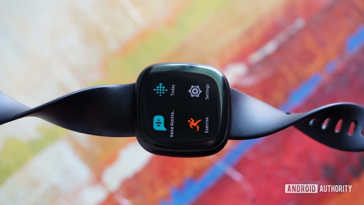 A Fitbit Versa 3 rests on an abstract, colorful background.