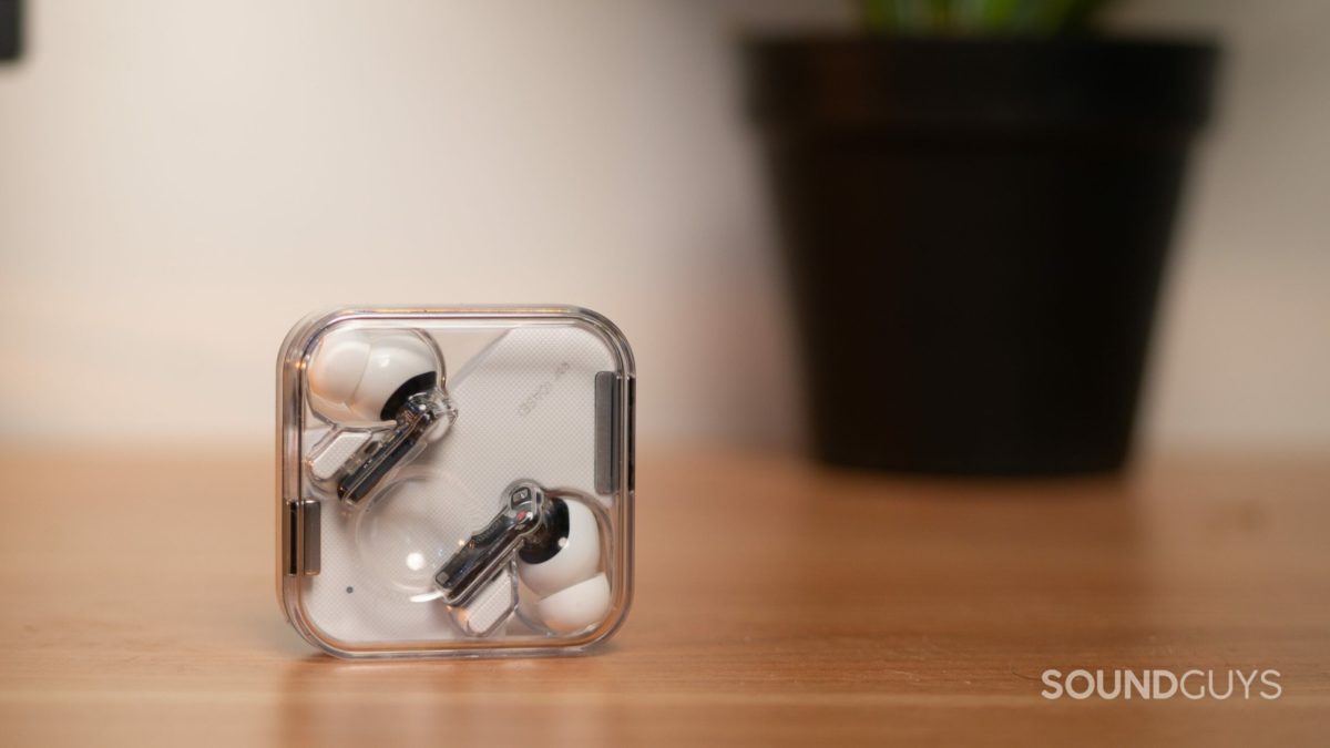 The Nothing Ear 1 true wireless earbuds rest in the clear case as it stands upright on a wood surface.