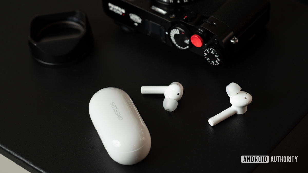 The OnePlus Buds Z cheap true wireless earbuds on a table next to a camera and the charging case.