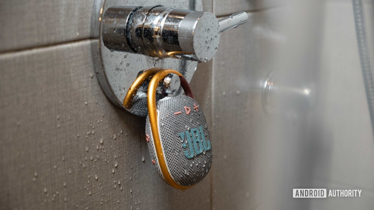 The JBL Clip 4 Bluetooth speaker hands from a shower as it's sprinkled by water.