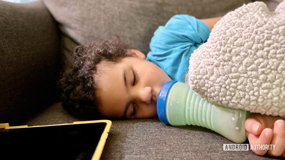 A toddler with a bottle and a blanket sleeping next to an iPad Air 2