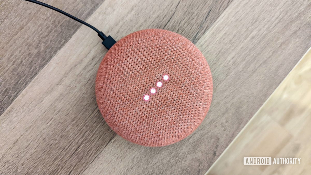 Google Home Mini in coral with lights on, on wooden background