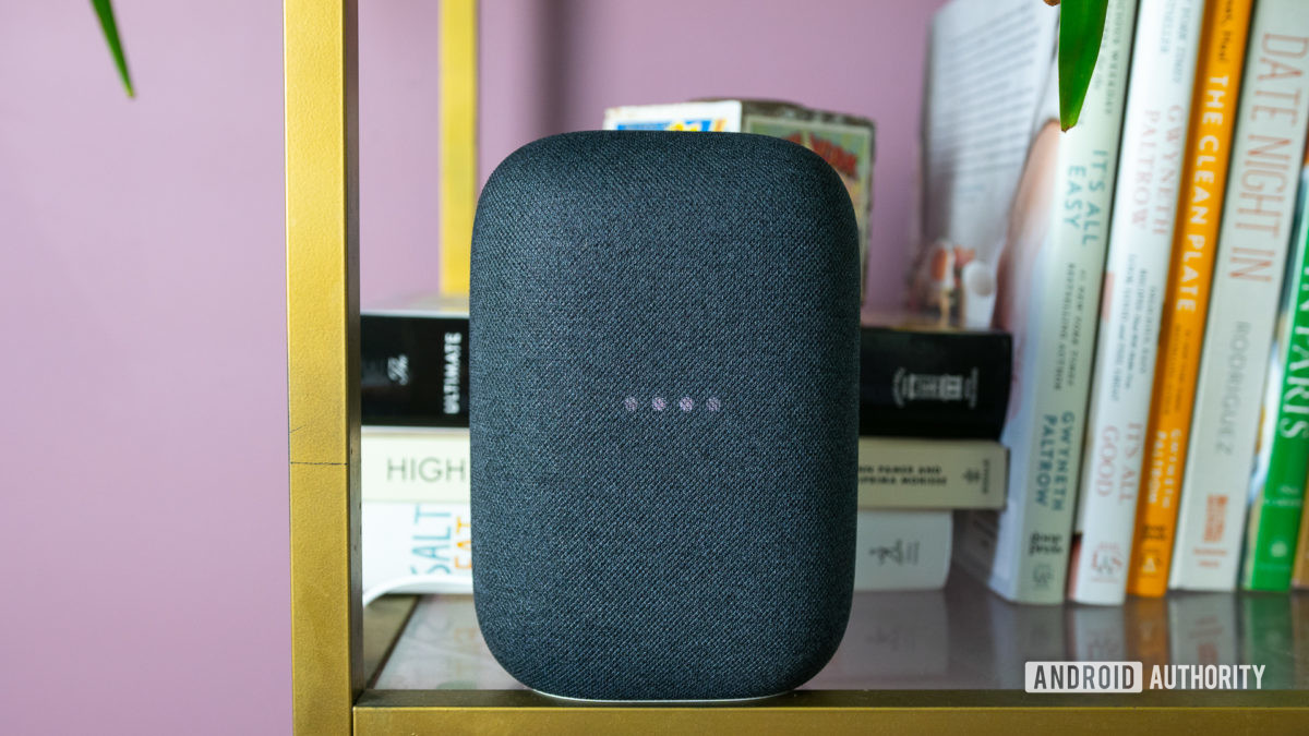 The gray Google Nest Audio on a bookshelf with the lights blinking.