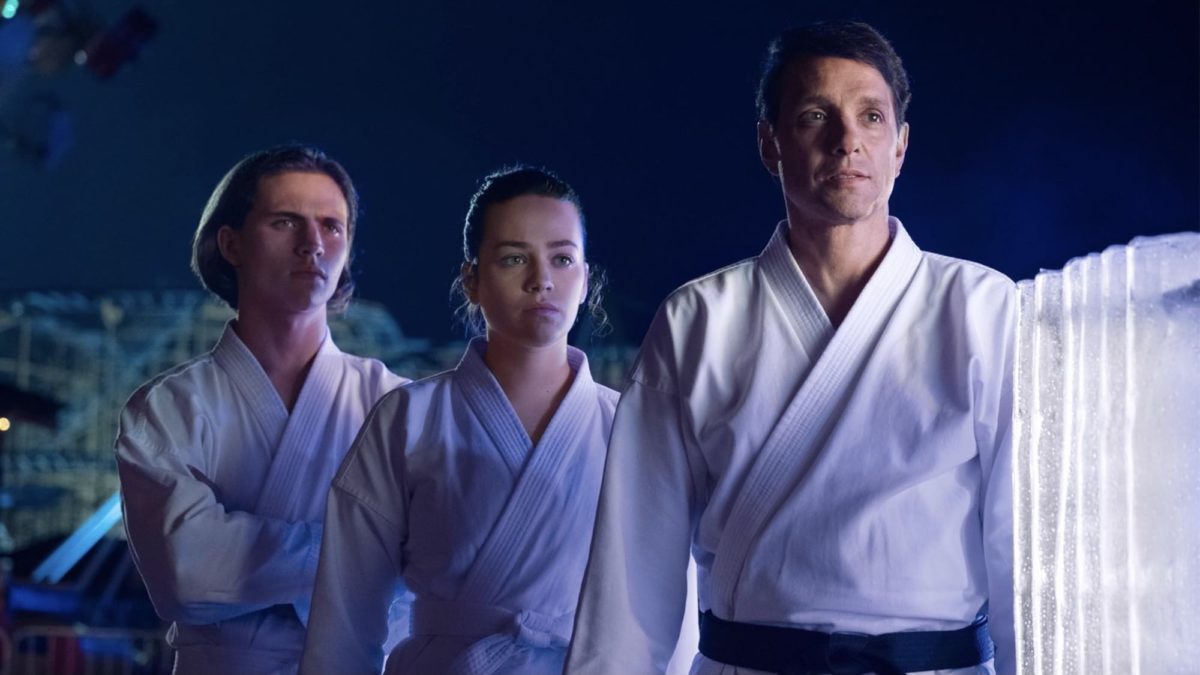 Ralph Macchio, Tanner Buchanan, and Mary Mouser stand together at night in Cobra Kai - best youtube originals