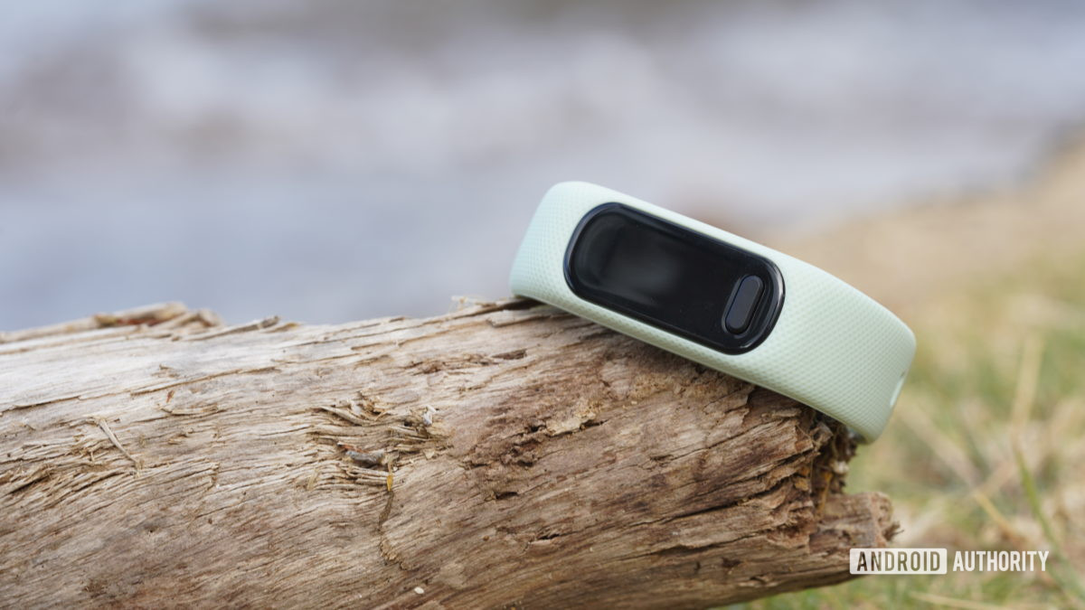 A Garmin Vivosmart 5 rests outdoors on a piece of driftwood.