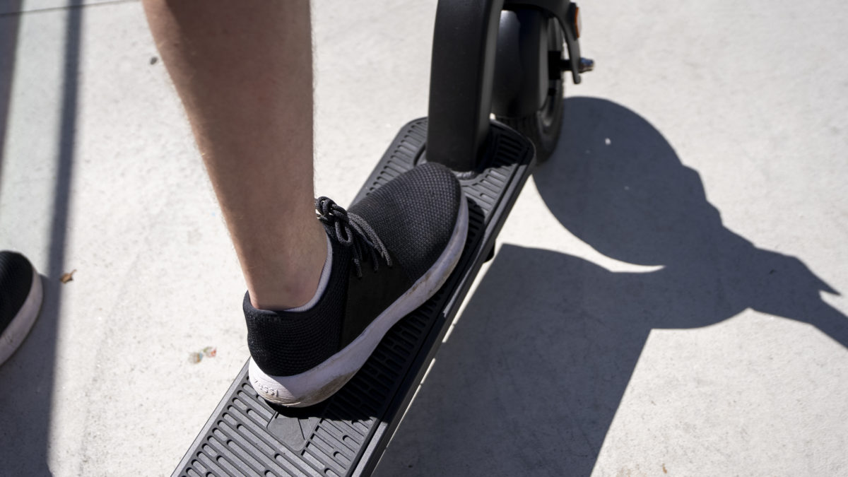 A foot in a black sports shoe, riding an electric scooter