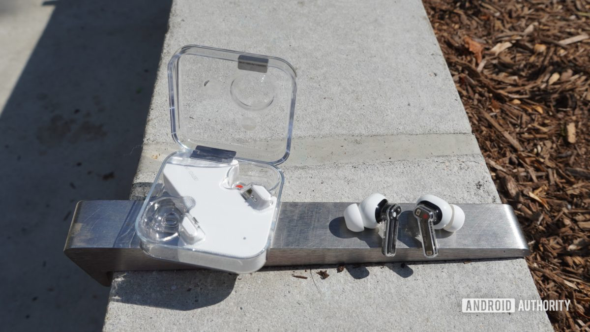 The Nothing Ear 1 buds sitting on a strip of metal next to their case.