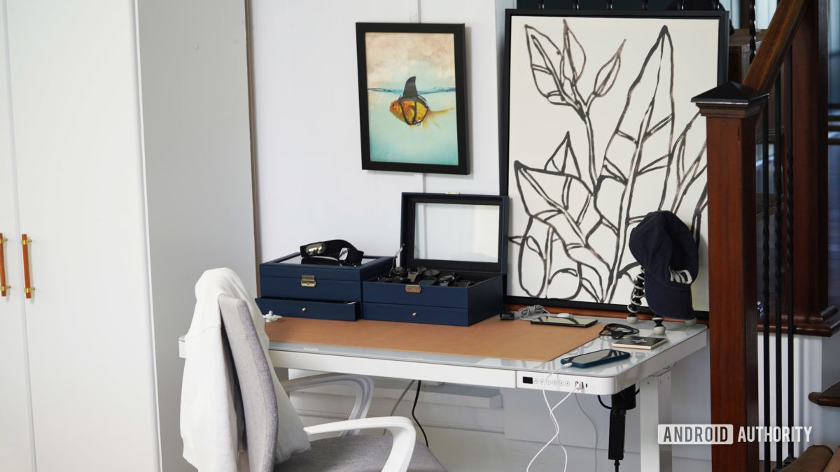 Two watch cases, two phones, and a collection of cables rest on a reviewer's desk.