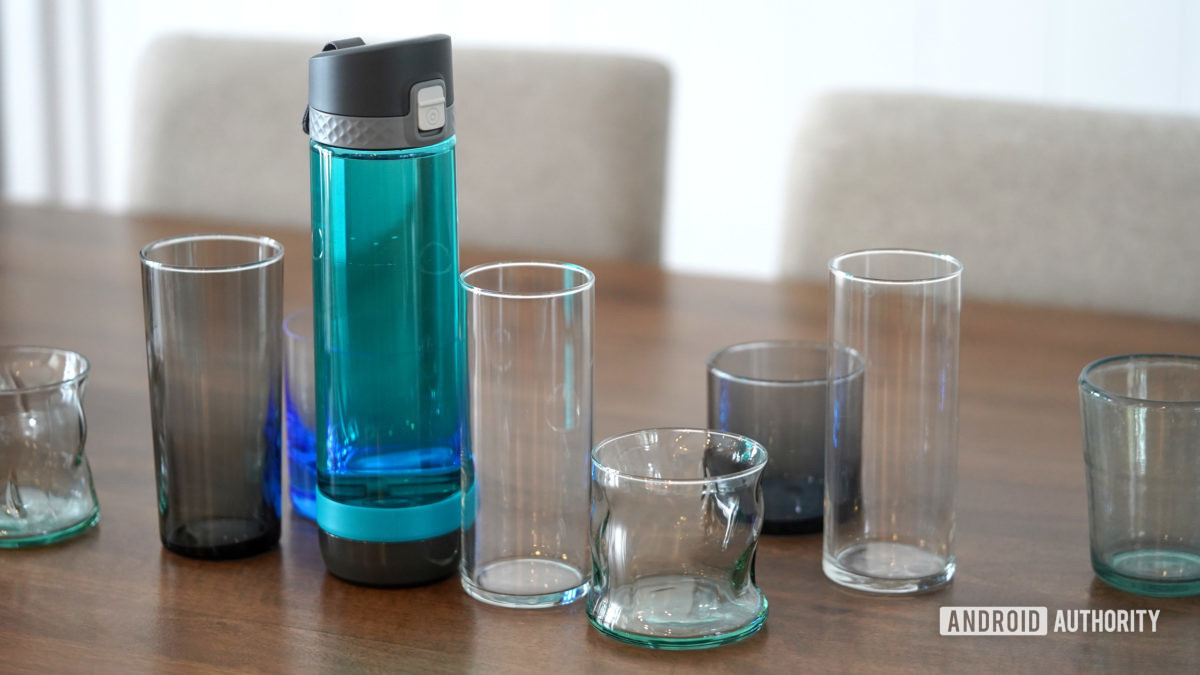 A smart water bottle stands among empty water glasses.