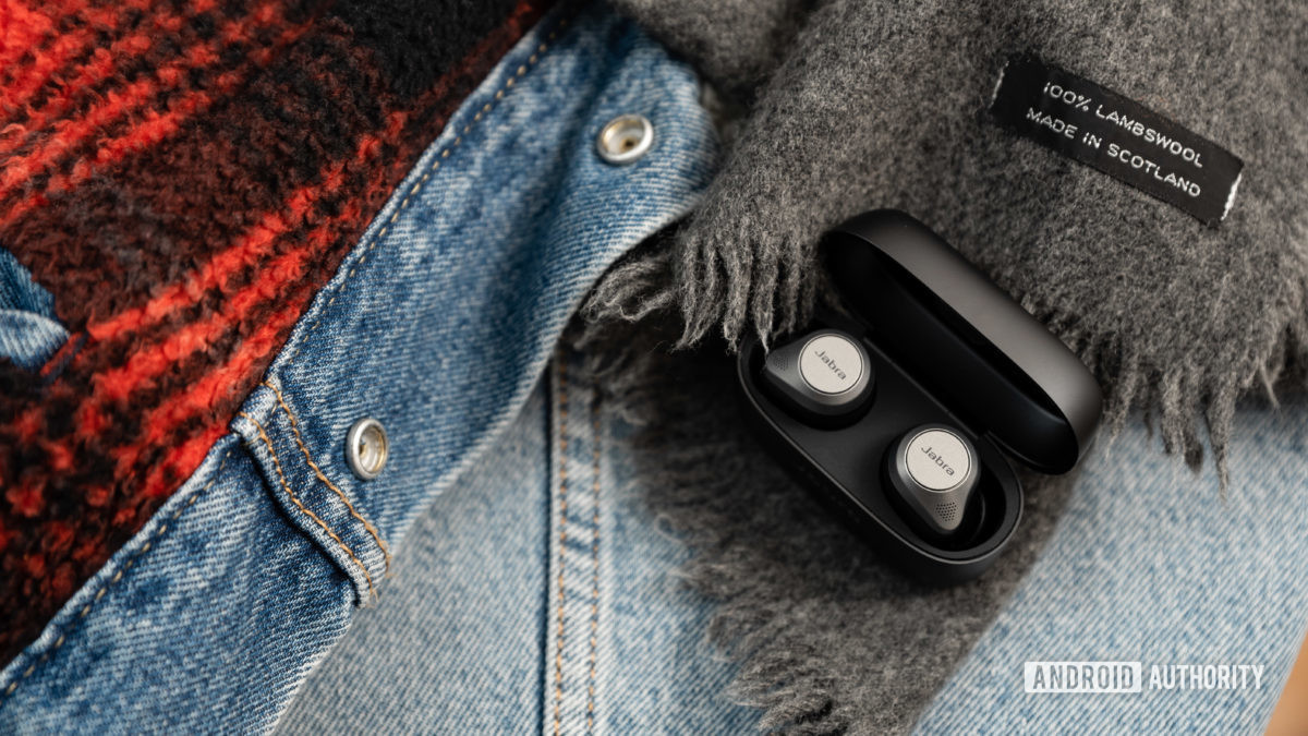 The Jabra Elite 85t noise cancelling true wireless earbuds in an open case and on top of a denim jacket.