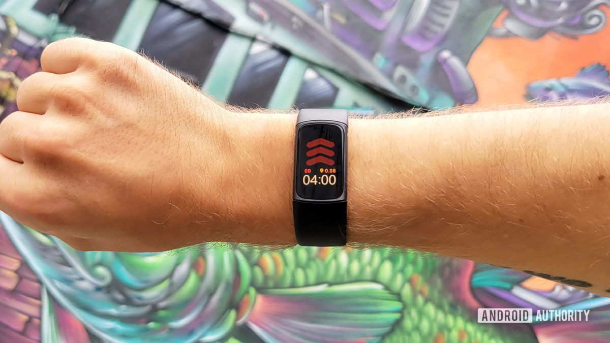 A user models the Fitbit Charge 5 in front of a painted mural wall.