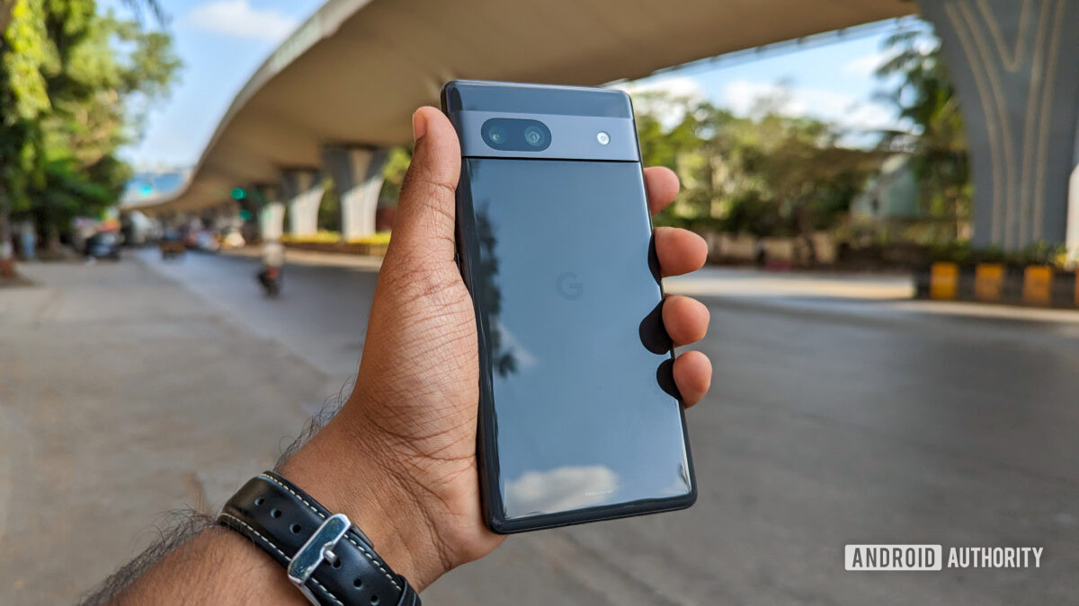 Google Pixel 7a held out in hand, with a city street and bridge in the background