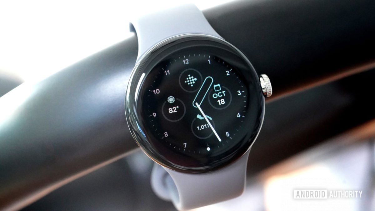 A Google Pixel Watch hangs from a stationary bike displaying the Classic watch face.