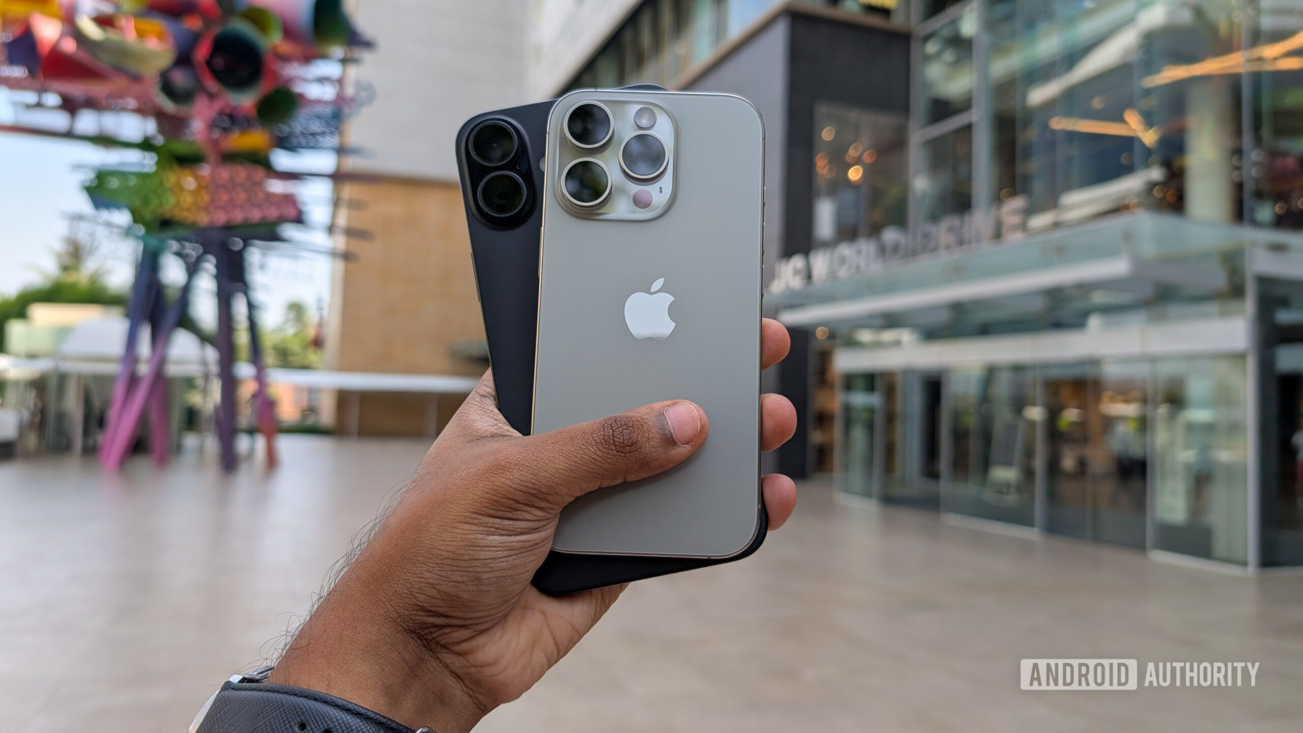 Apple iPhone 16 Plus in black color and iPhone 16 Pro in Natural Titanium color held out in hand