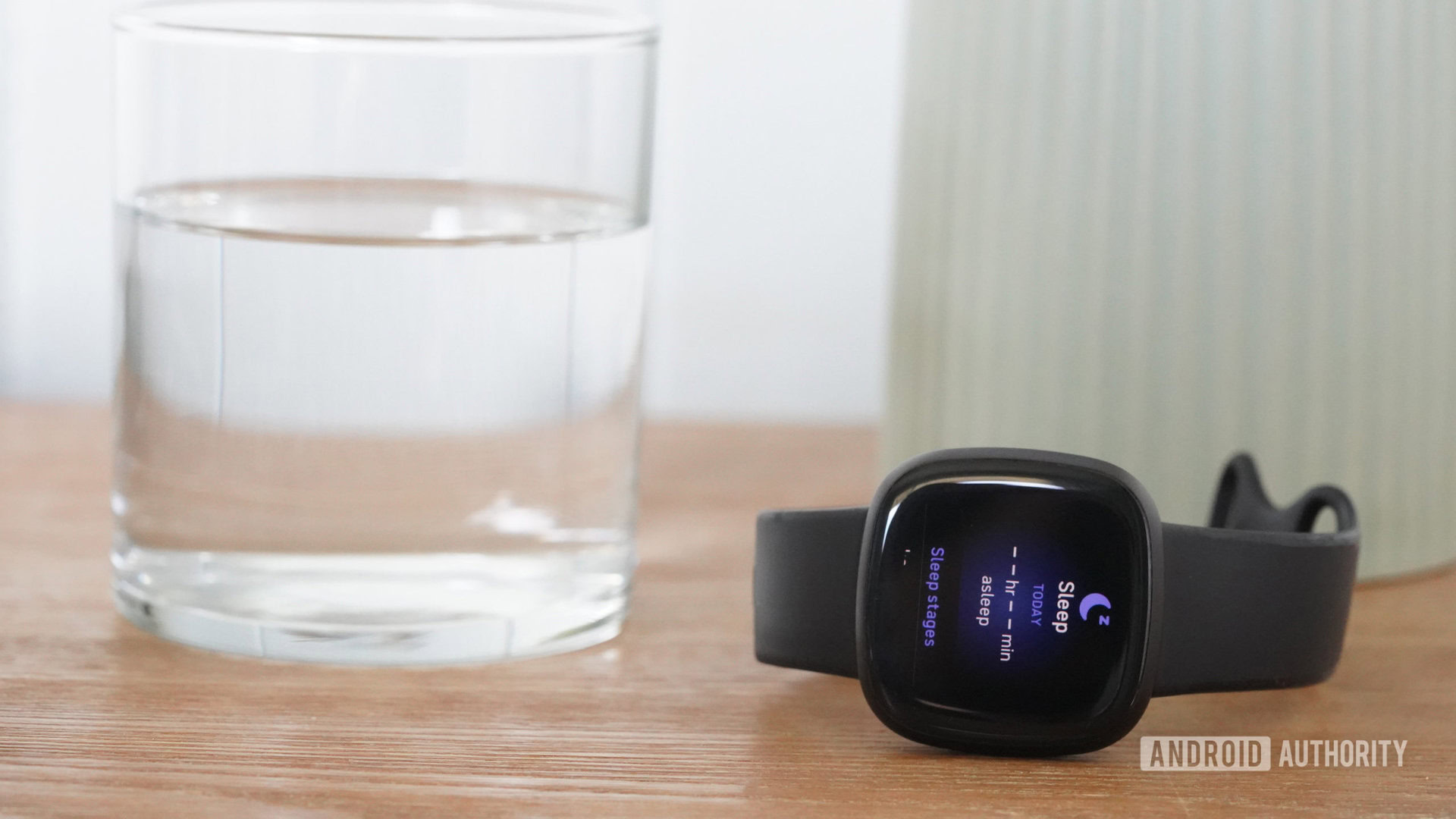 A Fitbit Versa 3 displays empty Sleep Data fields while resting on a bedside table.