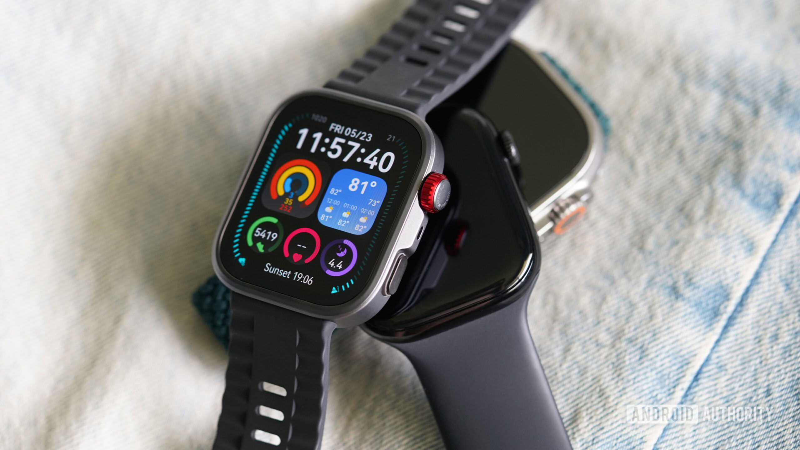 A Huawei Watch Fit 4 Pro rests on a couple of Apple Watches.
