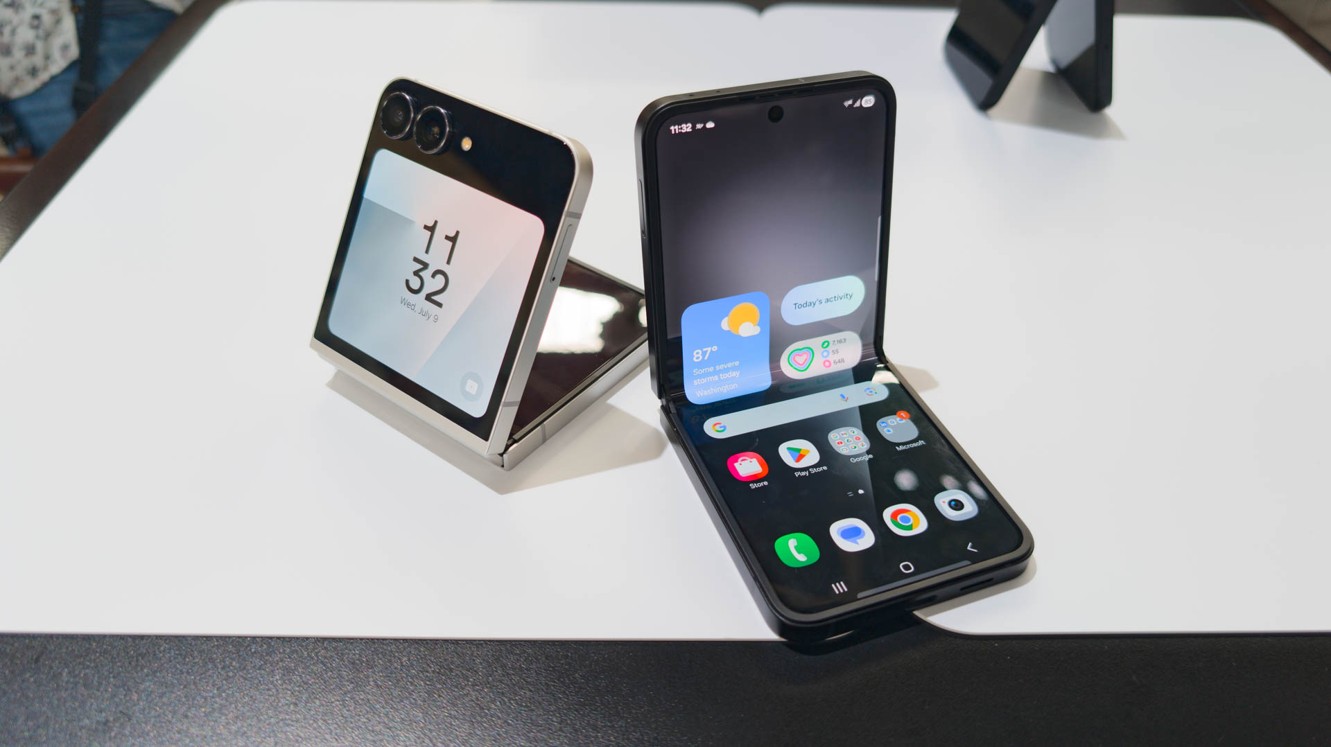 Samsung Galaxy Z Flip 7 FE in both Black and White colorways unfolded partially on table Samsung Galaxy Z Flip 7 FE in both Black and White colorways unfolded partially on table
