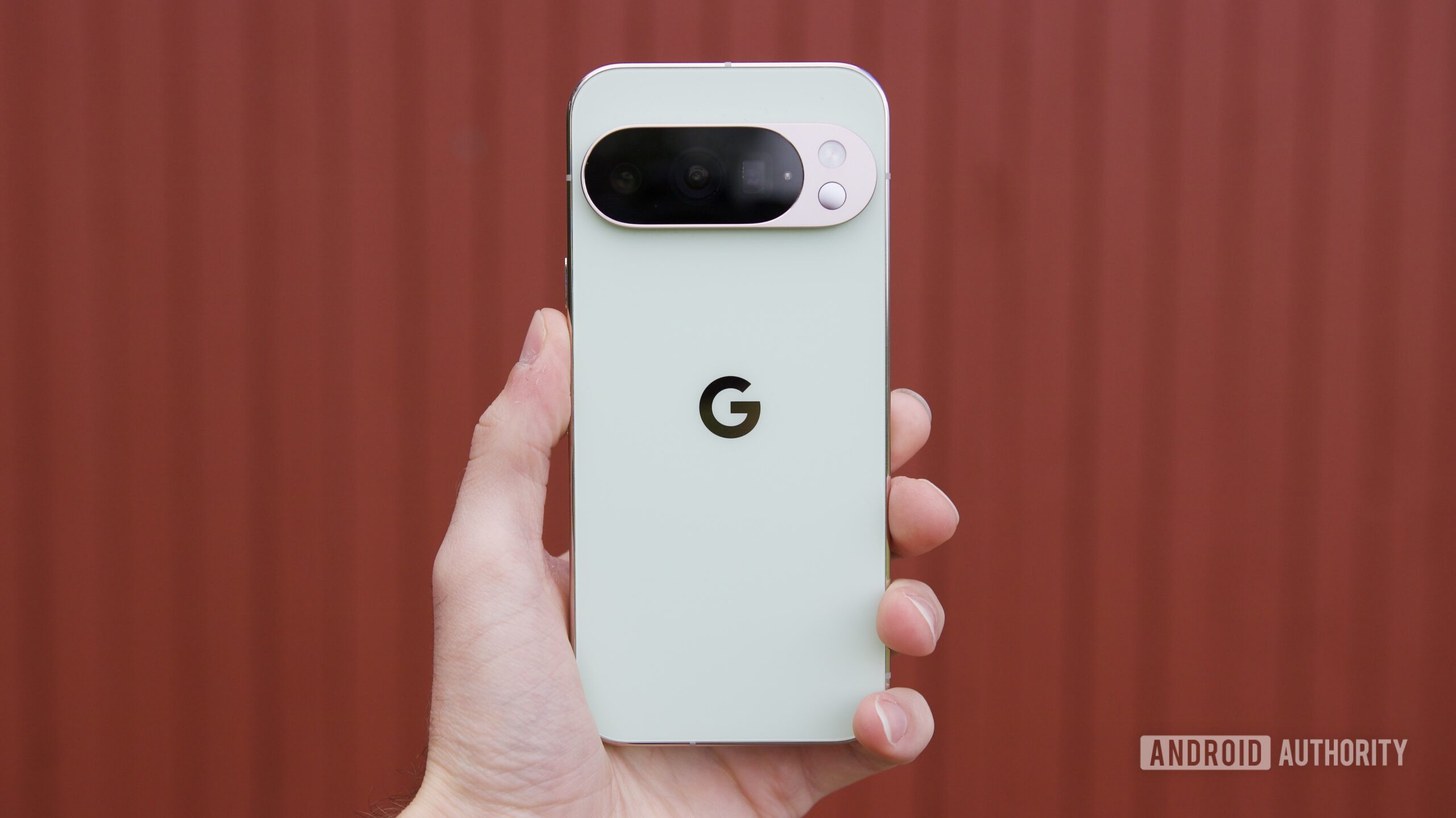 Someone holding the Google Pixel 10 Pro against a red background.
