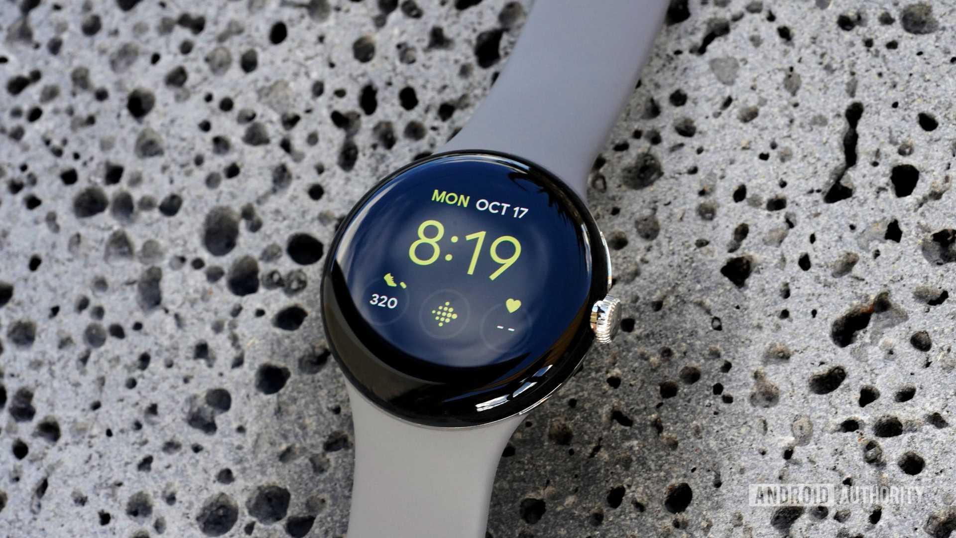 Google Pixel Watch Utility Face A Google Pixel Watch rests on a lava rock displaying the Utility watch face with a Fitbit shortcut.