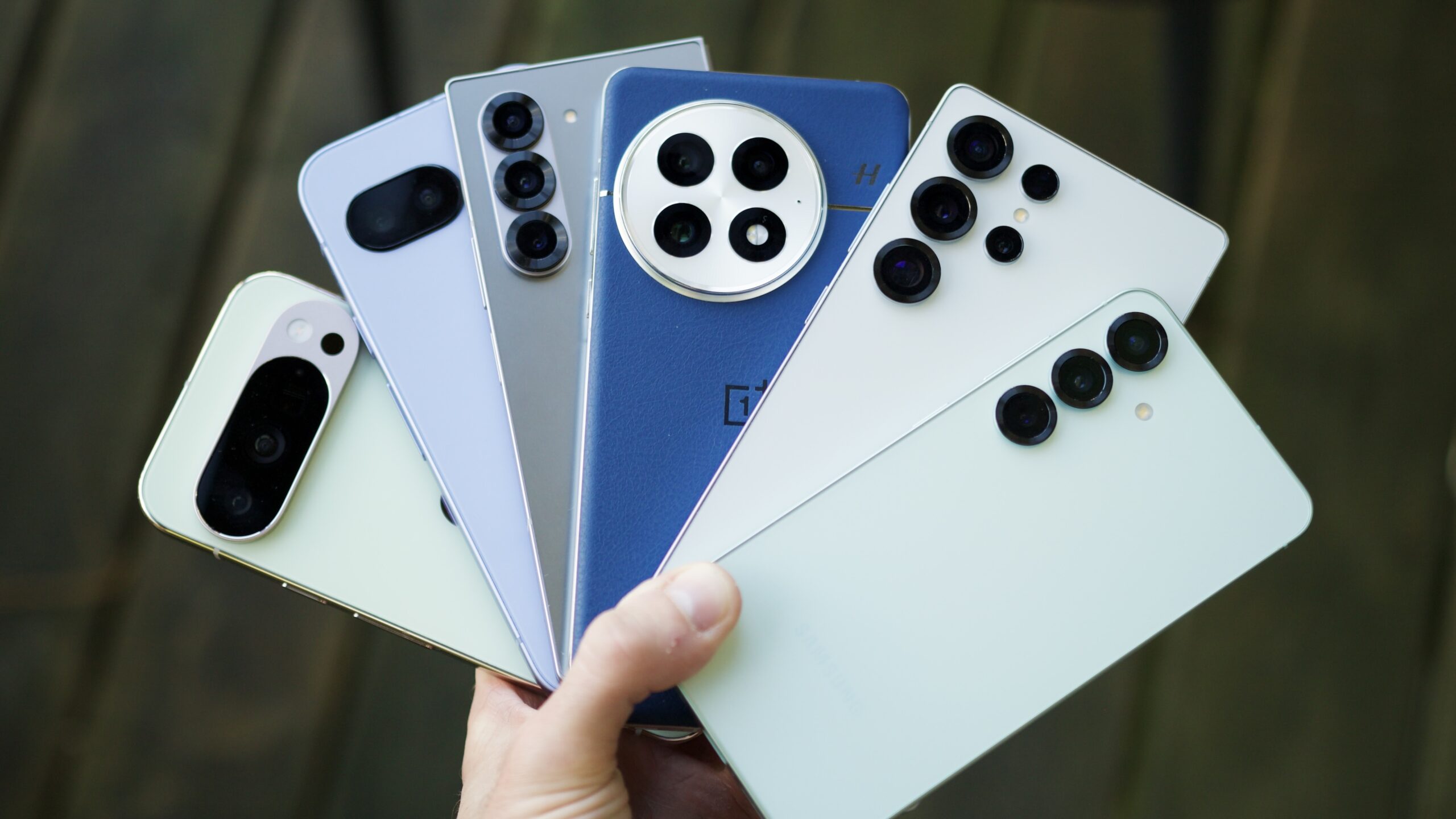 Someone holding a lot of Android phones, including ones from Google, Samsung, and OnePlus.