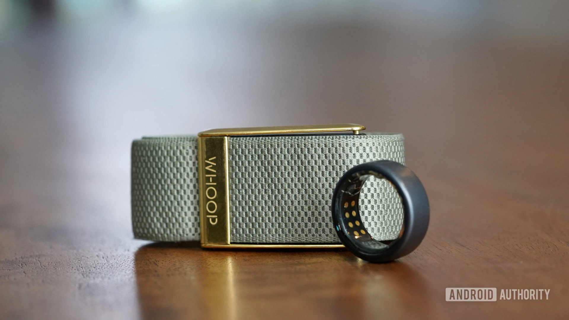 An Oura Ring 3 and Whoop 4 rests side by side on a wooden surface.